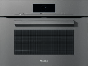 Front view of a Miele built‑in oven with a circular clock display, control strip, and long handle on a metallic door (kitchen appliance).