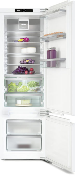 Tall white refrigerator with both doors open, revealing shelves of fruits, vegetables, eggs, and bottles inside and on the door.