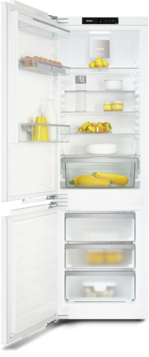 Open white refrigerator showing shelves with lemons, peppers, bottles, and a fruit bowl; bottom freezer drawers visible.