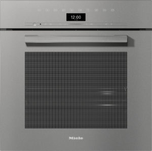 Front view of a Miele built-in appliance with a digital clock showing 12:00, control icons along the top, and a large perforated vent panel (logo at bottom).