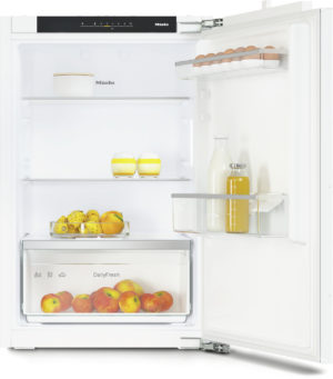 Open refrigerator showing eggs on the door shelf, a milk bottle, and a bottle of juice with fresh fruit in the crisper drawer below.
