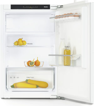 Open white refrigerator interior with eggs on the door rack, a bowl of lemons and oranges, milk and juice bottles on the shelf, and two yellow zucchini in the crisper drawer.