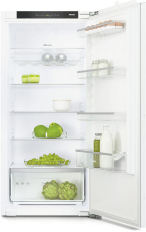 Open white refrigerator with organized shelves: green apples in a bowl on the upper-middle shelf, grapes in a drawer, artichokes in the bottom crisper, eggs and jars on the door shelves.