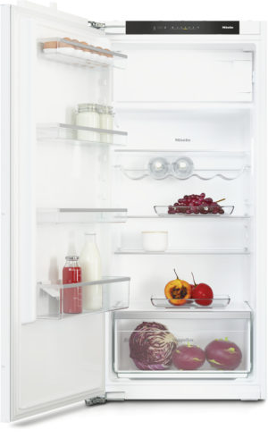 Open white refrigerator displaying eggs, milk, juice bottle, grapes, peppers, tomatoes, and a cabbage in the veggie drawer