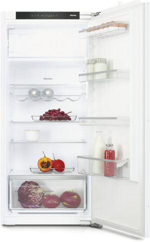 Open refrigerator showing fresh produce: grapes, tomatoes, persimmons, cabbage, milk and jars on clear shelves and door racks.