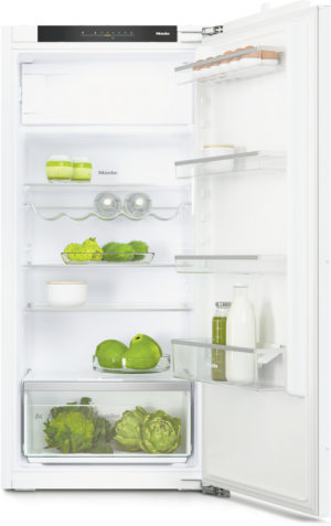 Open white Miele refrigerator with eggs on the door rack, bottles of dairy on the shelves, apples and greens in the middle, and artichokes in the bottom vegetable drawer.