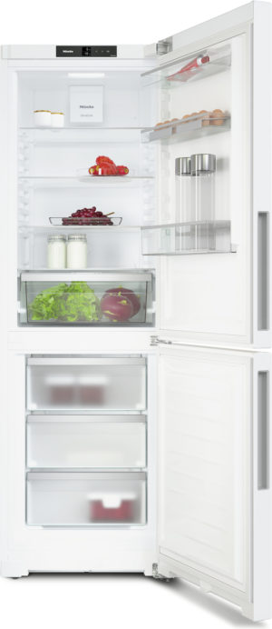 Open white refrigerator with upper fridge and lower freezer. Shelves hold milk, grapes, lettuce, tomatoes, eggs, and jars; interior light on.