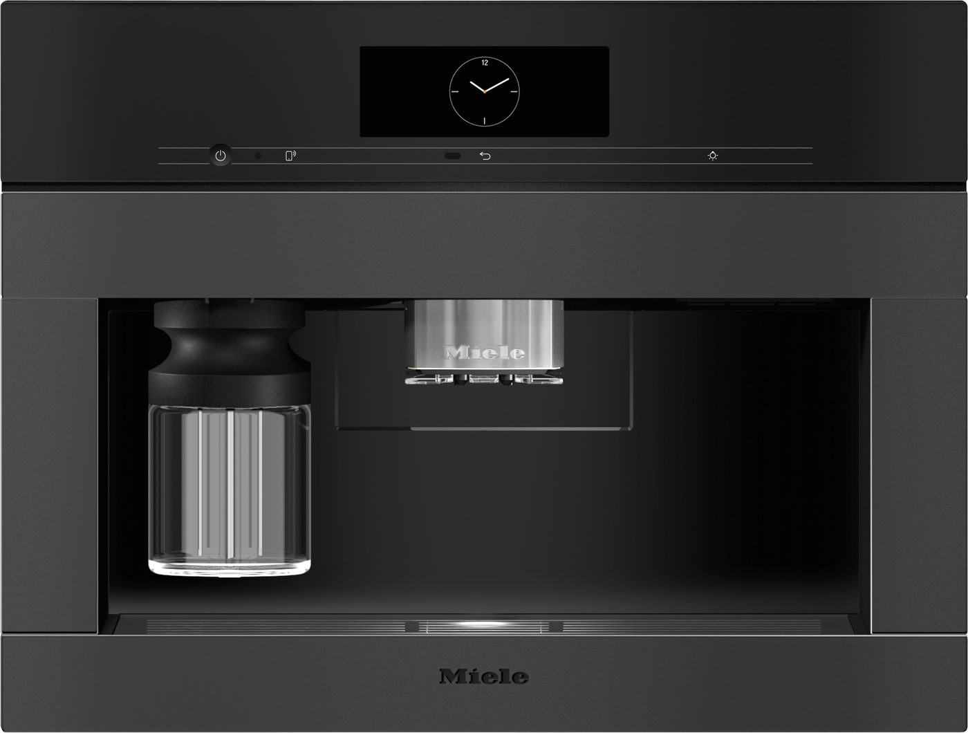Miele built-in coffee machine with a black front, metal brew group center, and glass carafe on the left.