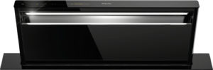 Black built-in oven with glossy finish, chrome handle, and top control panel (Miele branding) showing an illuminated interior through the glass door.