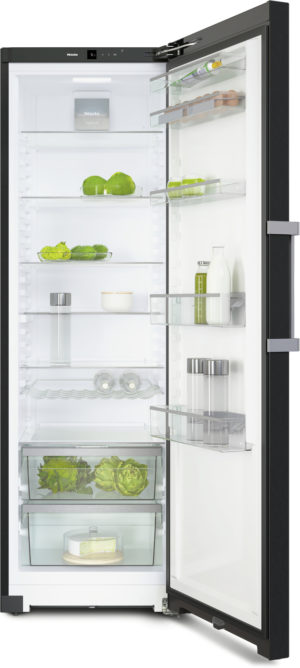 Open refrigerator with fresh produce on shelves, eggs and bottles on the door, and a cake on the bottom drawer.