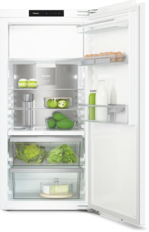 Open white refrigerator showing eggs on the upper shelf, jars, milk bottle, greens, and a cake in the bottom drawer.