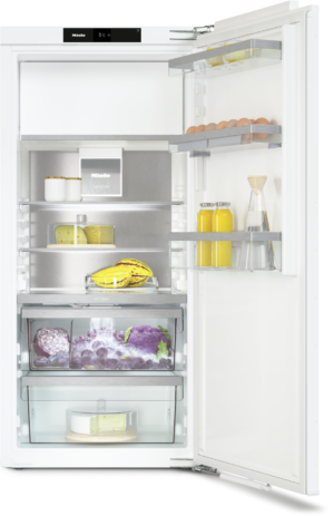 Open fridge with eggs on the door, juice bottles, cheese blocks, bananas, and a produce drawer with grapes and purple cabbage.