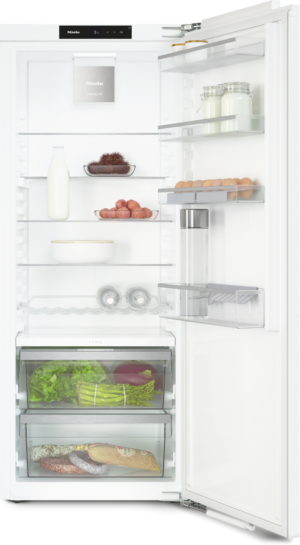 Open refrigerator showing milk on a left shelf, eggs on a right shelf, jars, and fresh produce in lower drawers.