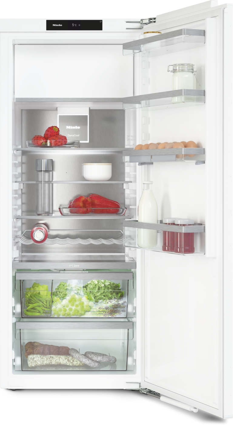 Open refrigerator door showing organized shelves: dairy and jars on the upper shelves, peppers and fruit mid-level, greens and grapes in the drawer, and bread and sausages in the bottom bin.