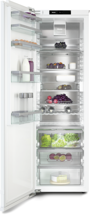 Open modern refrigerator filled with milk, juice, eggs, berries, grapes, lettuce, and a cake, organized on glass shelves and crispers.