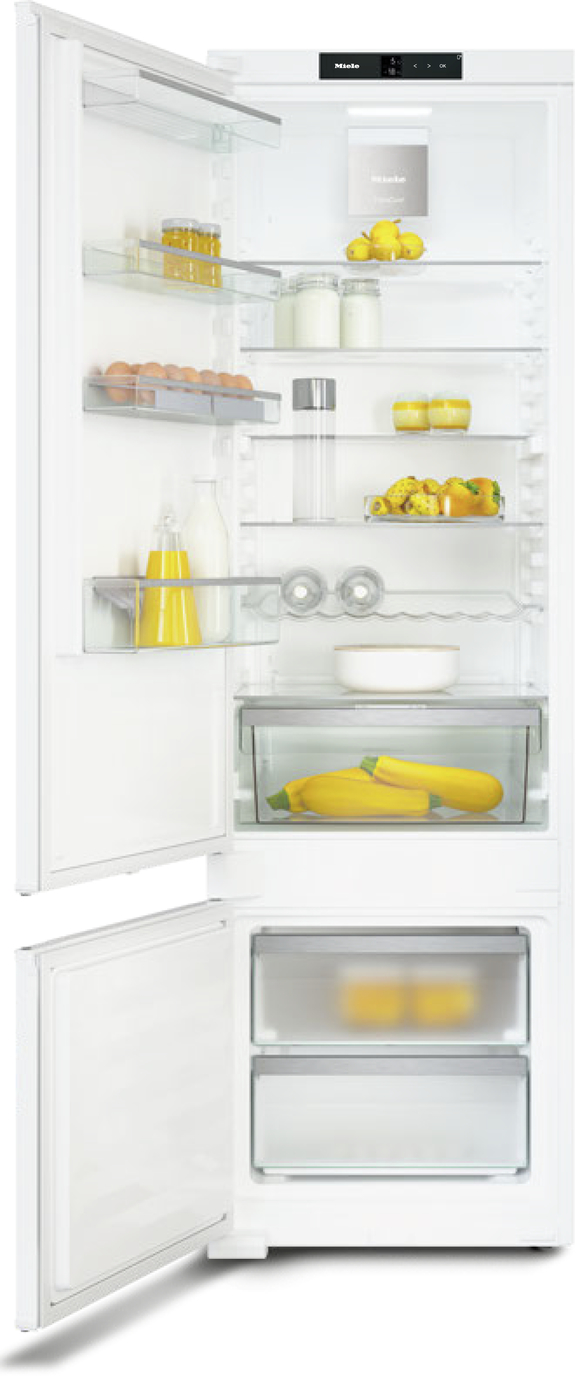 Open white refrigerator showing milk, eggs, lemons, peppers, and juice on glass shelves and door compartments.