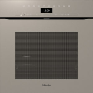 Miele built-in oven front with a digital clock showing 12:00 and a textured glass panel, set in a beige kitchen.