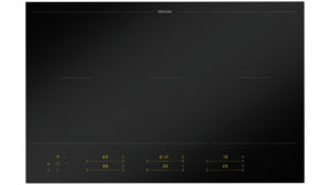 Induction cooktop with sleek black glass surface and touch controls at bottom, glowing yellow indicators on knobs.