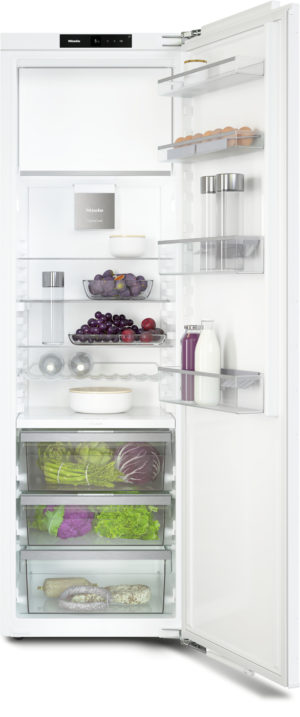 Open white refrigerator with shelves holding eggs, dairy, fruits, vegetables, and drinks in a bright kitchen system.
