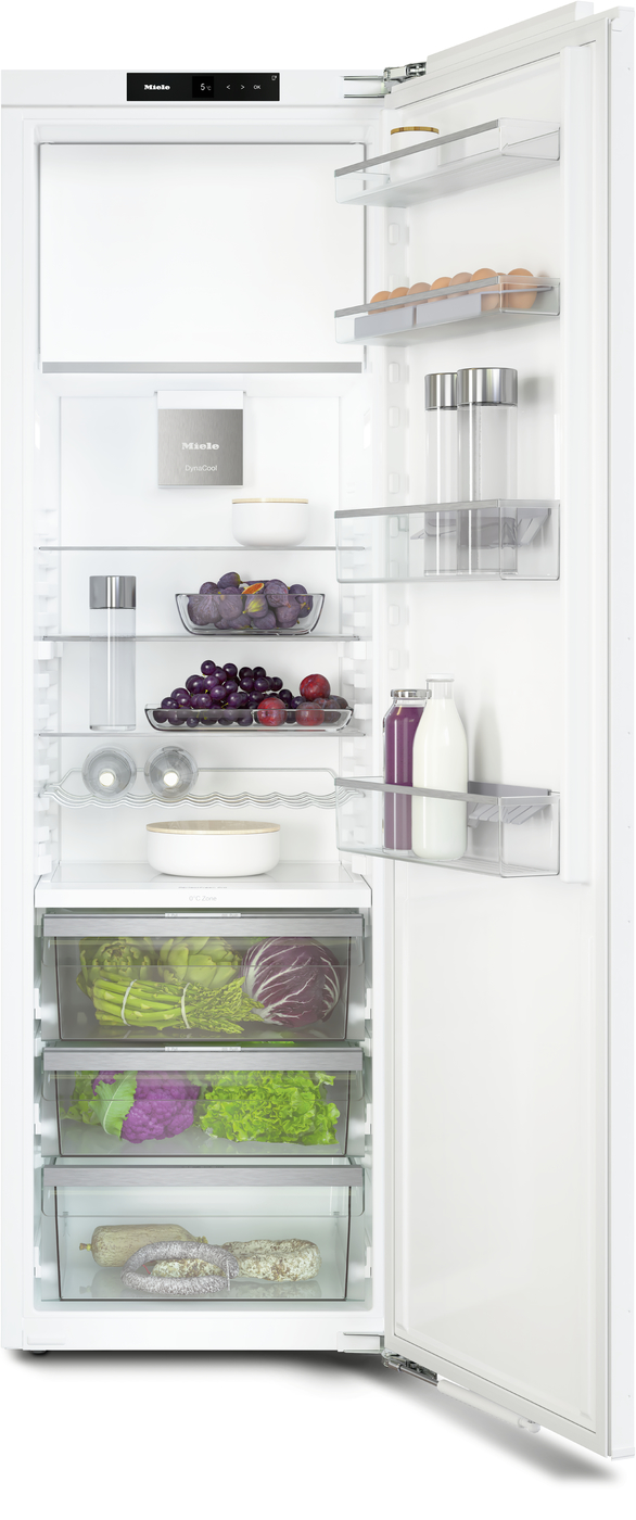 Open white refrigerator with shelves holding eggs, dairy, fruits, vegetables, and drinks in a bright kitchen system.