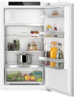 Open Siemens refrigerator showing upper shelves with jars and condiments, middle shelf with sauces, lower drawer full of fresh produce like lettuce, apples, pears, and broccoli visible at the bottom.