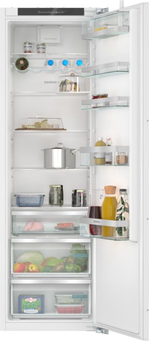 Open Siemens refrigerator with multiple shelves and door racks; contains juice bottles, dairy, condiments, cheese and cake, a pot, and fresh produce in the bottom drawer.