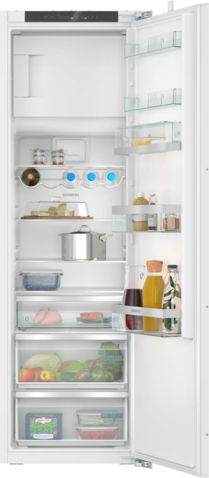 Open white Siemens fridge showing internal shelves, slide-out door shelves, a bottom freezer with produce and bottled drinks, and a large pot on the middle shelf.