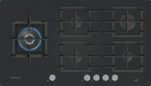 Siemens gas cooktop with several burners; the left burner is lit with a blue flame and control knobs along the bottom edge.