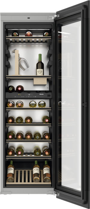 Open wine refrigerator filled with bottles on wooden shelves and a few glasses inside.”, "Tall wine cooler with glass door, multiple shelves of wine bottles and a small box nearby in the middle.", "Interior of a wine fridge showing numerous bottles on shelves with a couple of glasses.", "Wine cooler with door open, bottles arranged on racks and bottles resting on a wooden crate at the bottom."