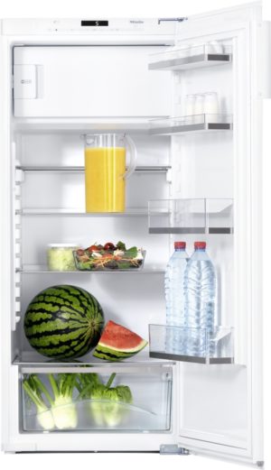 Open fridge showing fresh produce and drinks: pitcher of orange juice, salad bowl, watermelon, greens, and bottled water on shelves and door.