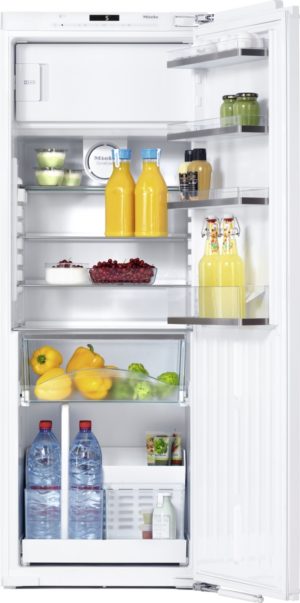 Open refrigerator with two orange juice bottles centered on the middle shelf, berries, peppers, greens, and drinks visible on other shelves.