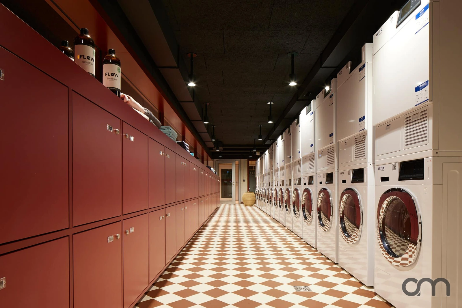 Buanderie collective d'immeuble équipée d'une rangée de colonnes lave-linge et sèche-linge Schulthess, configuration courante des PPE et gérances du canton de Neuchâtel
