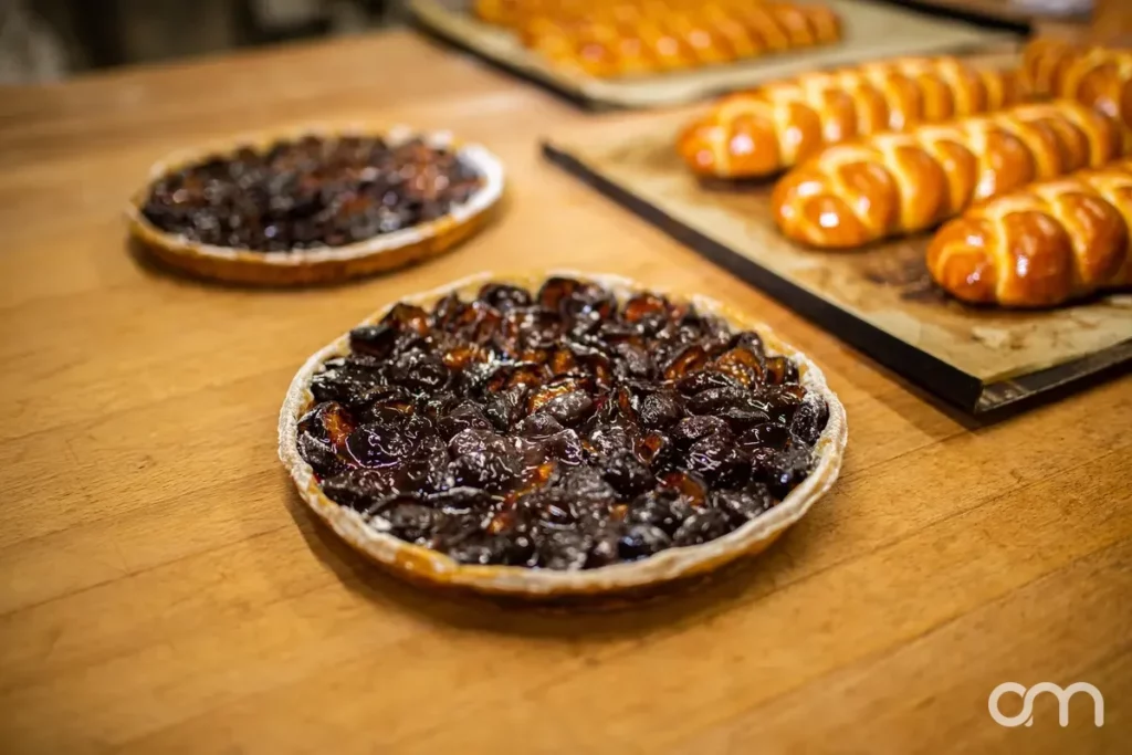 Deux tartes aux pruneaux artisanales refroidissant sur un plan de travail en bois, tresses au beurre en arrière-plan