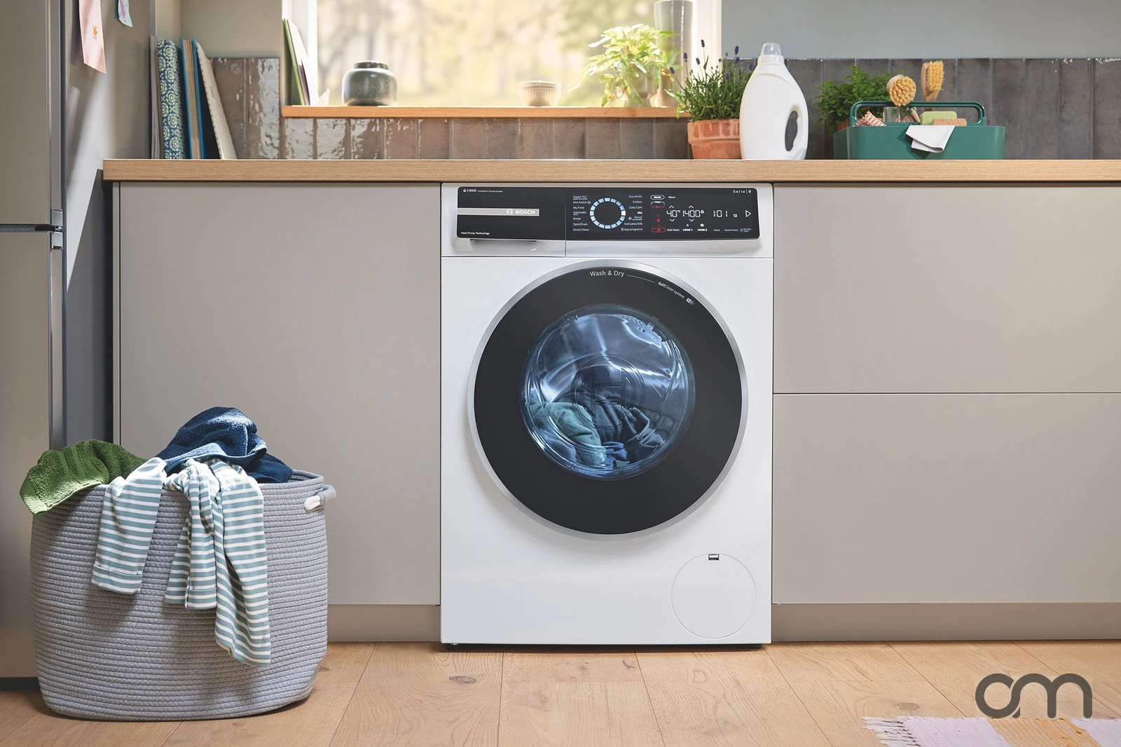 Lave-linge séchant Bosch Série 8 à pompe à chaleur installé sous un plan de travail en bois, panier de linge à côté : lave-linge séchants vendus et posés par Arts & Ménagers dans le canton de Neuchâtel