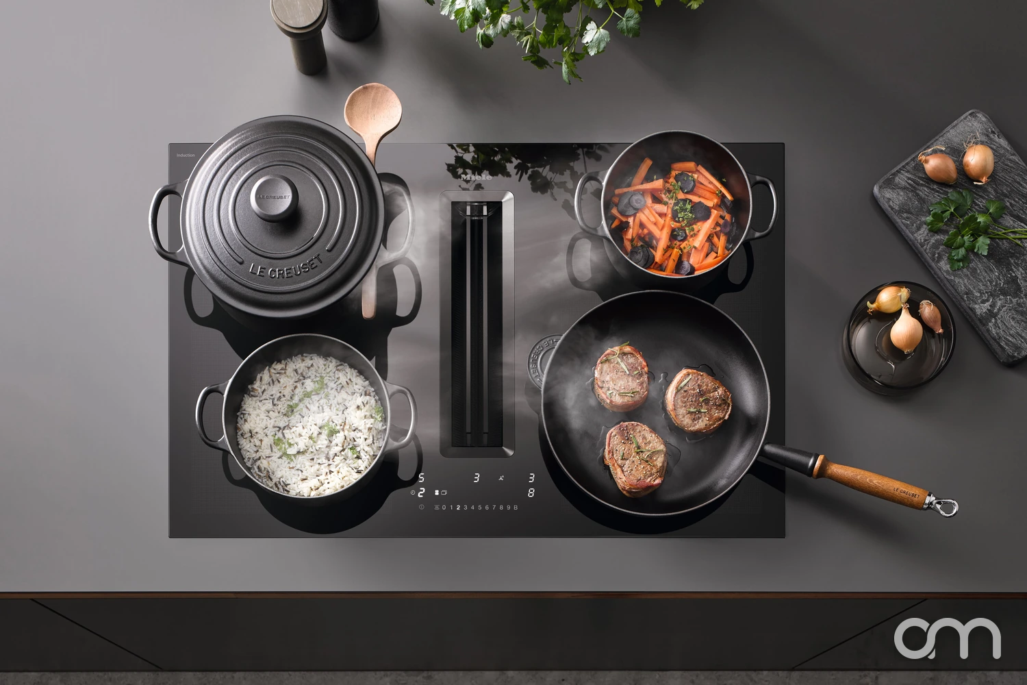 Vue de dessus d'un plan de cuisson à induction Miele avec hotte intégrée : cocotte, casserole de riz et poêlée en cours de cuisson