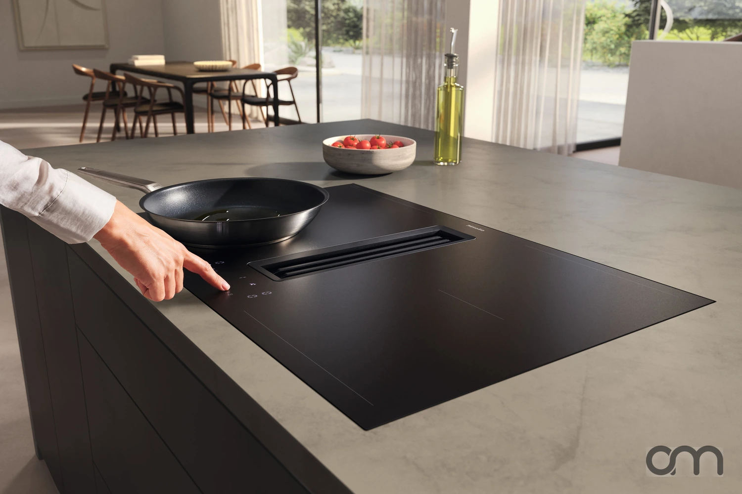Main réglant le bandeau tactile d'un plan de cuisson à induction affleuré sur un îlot de cuisine, dans une maison du canton de Neuchâtel